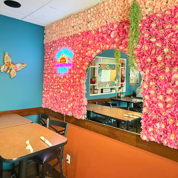 Vibrant Silly Serrano Mexican Restaurant interior with pink floral walls, a neon sign, and colorful decor.