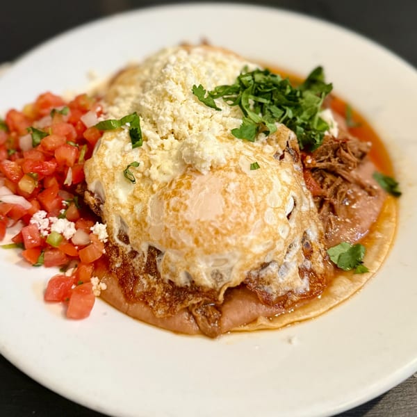 Huevos Rancheros with fried eggs, shredded meat, pico de gallo, and crumbled cheese on a white plate.