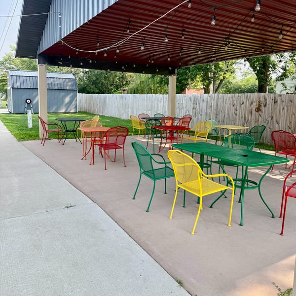 Outdoor patio with colorful red, yellow, and green metal tables and chairs under a red awning.