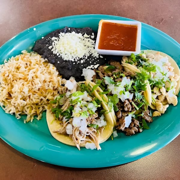 A vibrant plate of Silly Serrano Mexican tacos with rice, beans, and a side of red sauce.