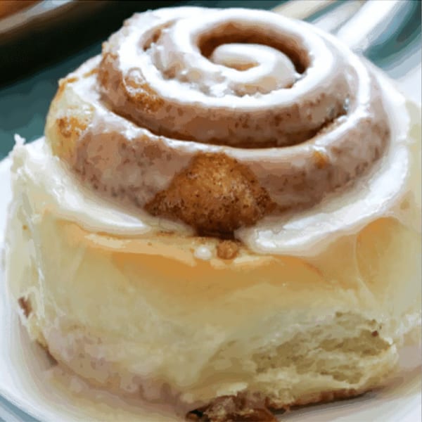 Close-up of a frosted cinnamon roll with a swirl of icing and a sprinkle of cinnamon sugar.