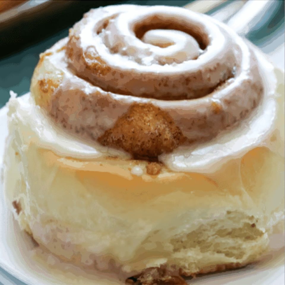 Close-up of a frosted cinnamon roll with a swirl of icing and a sprinkle of cinnamon sugar.
