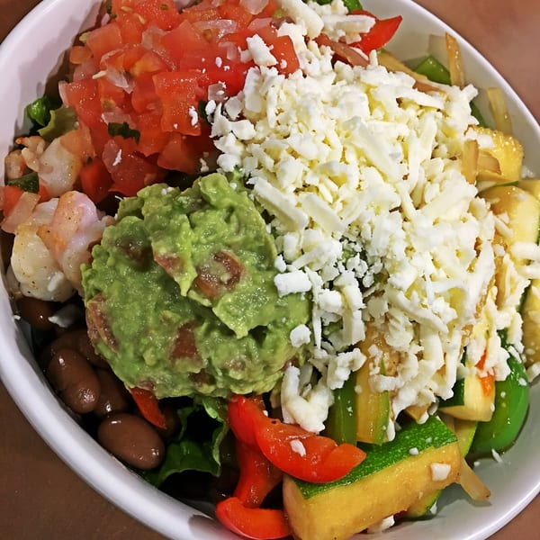 A vibrant Mexican bowl with guacamole, pico de gallo, cheese, shrimp, beans, and vegetables.