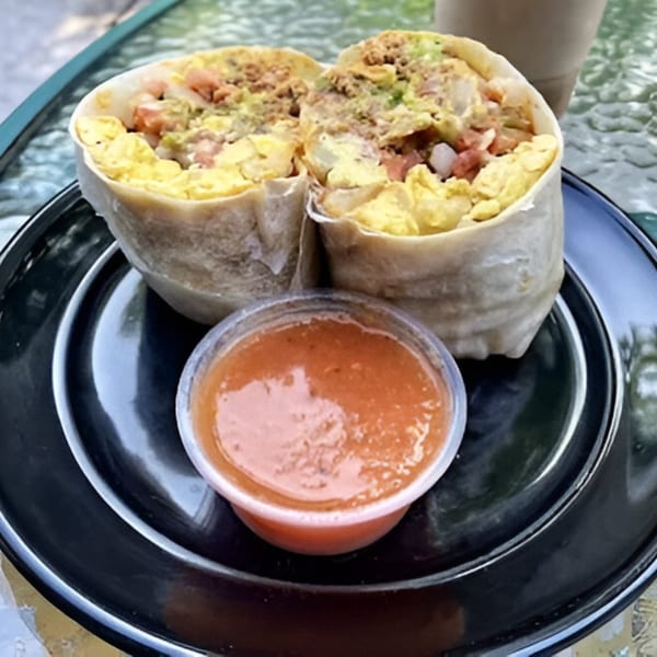 A breakfast burrito, cut in half, revealing eggs, potatoes, and salsa, served with a side of red salsa.