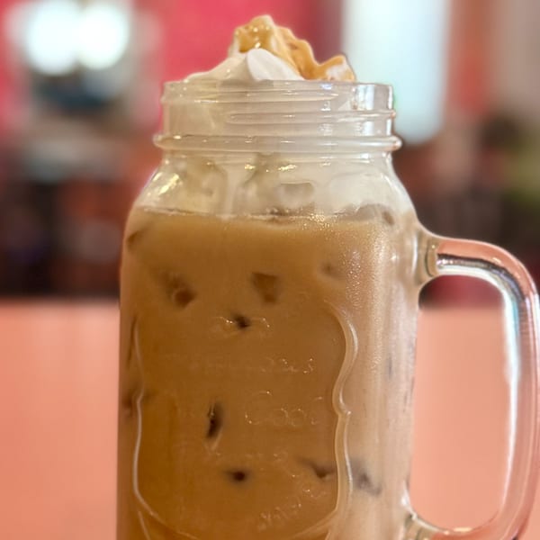 Iced coffee in a mason jar mug, topped with whipped cream and a caramel drizzle.