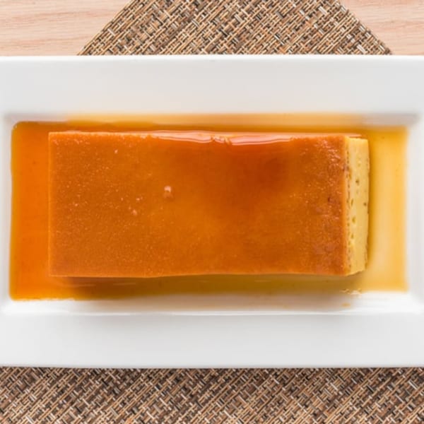 Rectangular flan dessert with caramel sauce on a white plate, on a woven placemat.