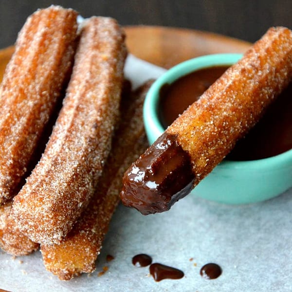 Crispy churros coated in cinnamon sugar, with one dipped in a teal bowl of rich chocolate sauce.
