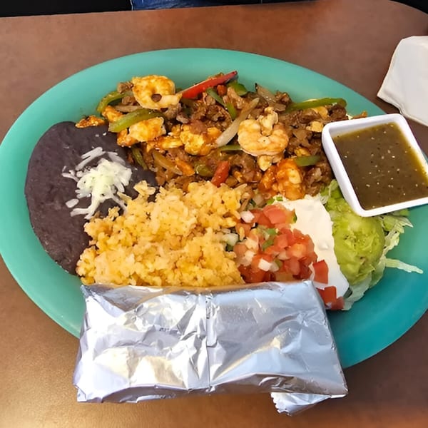 A vibrant Mexican combo plate with shrimp and beef fajitas, rice, beans, pico de gallo, and guacamole.