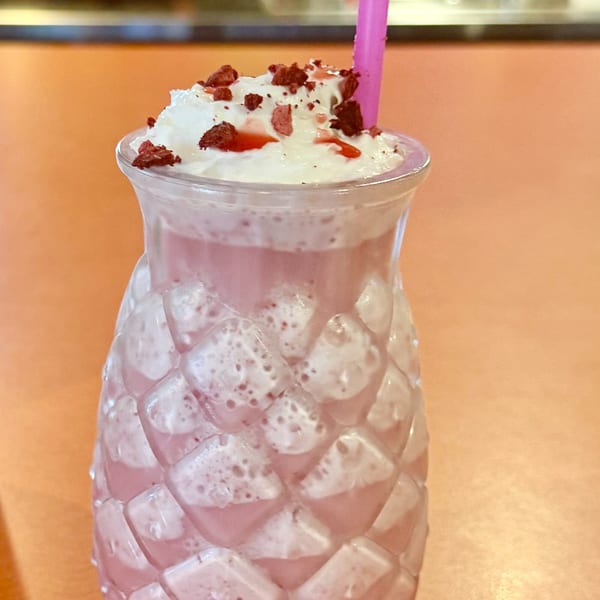 Pink drink with whipped cream, red sprinkles, and a pink straw in a textured glass.