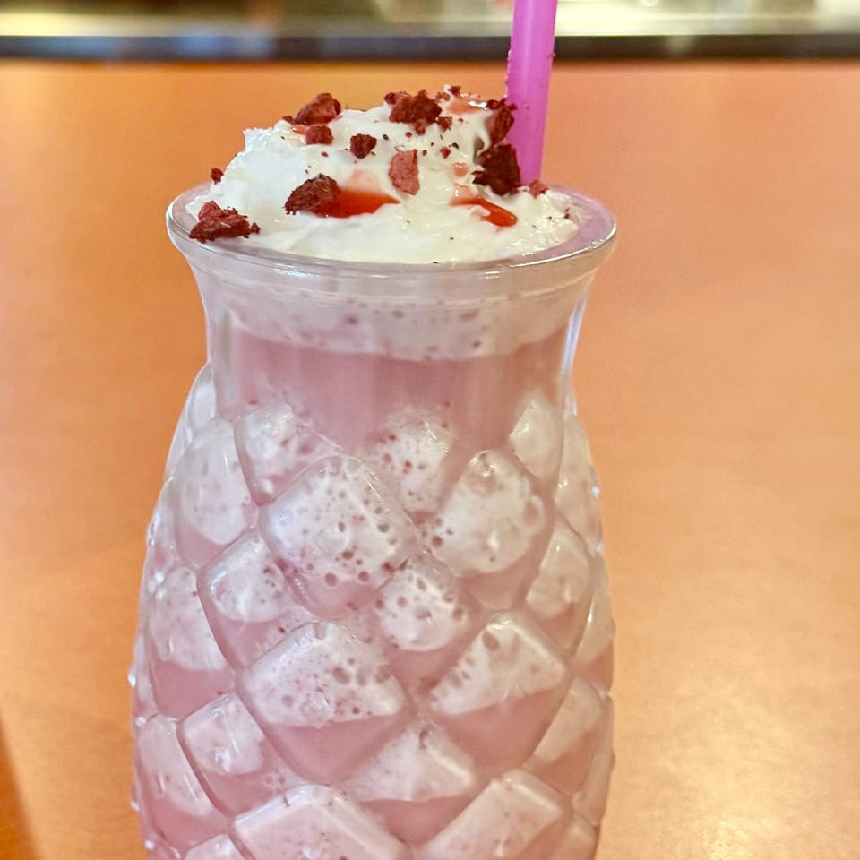 Pink drink with whipped cream, red sprinkles, and a pink straw in a textured glass.