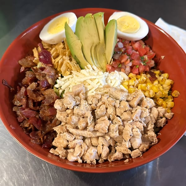 A vibrant Mexican salad in a red bowl, featuring chicken, bacon, corn, avocado, pico de gallo, and eggs.