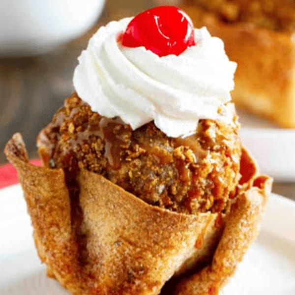 Fried ice cream dessert with whipped cream, a cherry, and caramel in a crispy tortilla bowl.