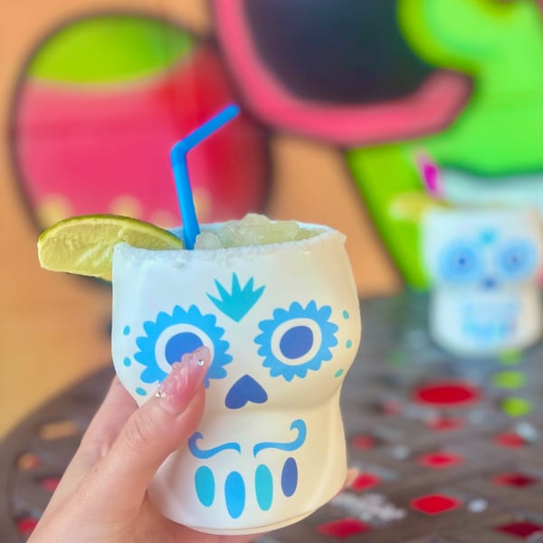Hand holding a Silly Serrano Mexican Restaurant margarita in a sugar skull mug with a lime.