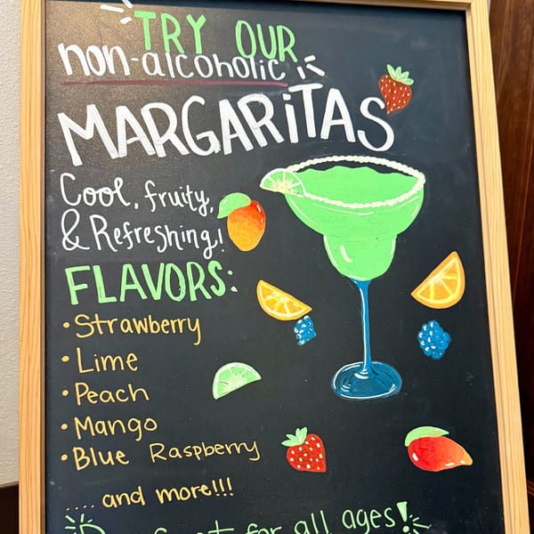 A chalkboard sign advertises non-alcoholic margaritas with various fruit flavors and illustrations.