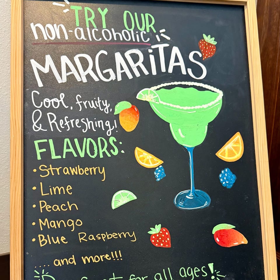 A chalkboard sign advertises non-alcoholic margaritas with various fruit flavors and illustrations.