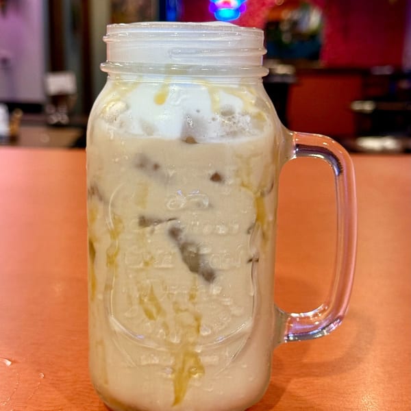 Horchata in a mason jar with ice and caramel drizzle on an orange table at Silly Serrano.