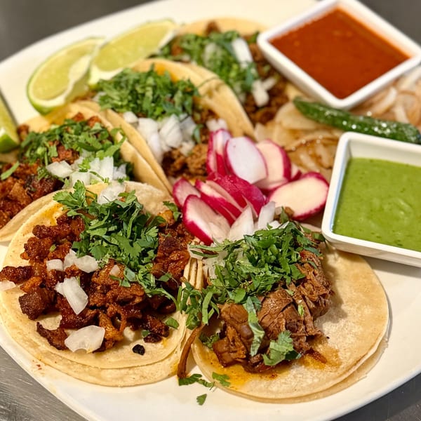 A platter of various Mexican street tacos with lime, radishes, and two dipping sauces.