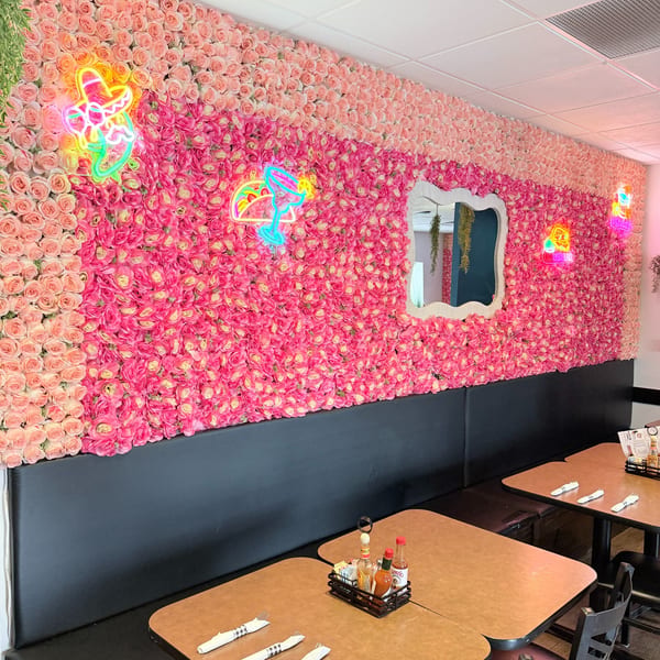 Pink and peach floral wall with neon Mexican-themed signs and a mirror above restaurant booths.